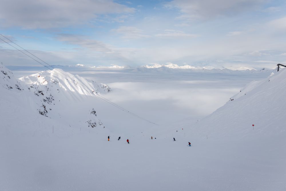 Vu du sommet d’une piste, sur une mer de nuages, on voit seulement dépasser les hauts massifs.