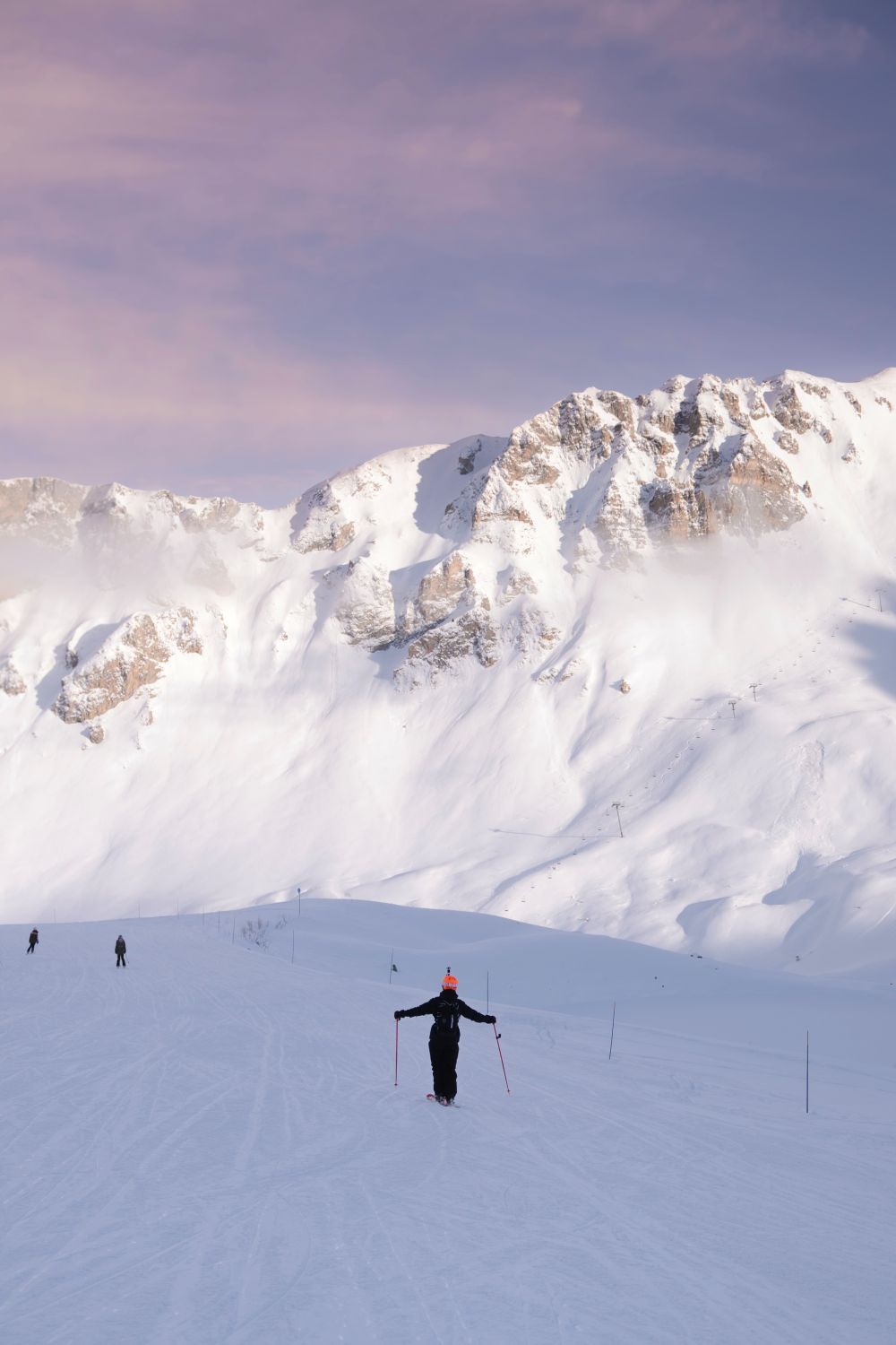 Skieur sur une piste enneigée face aux sommets majestueux des 3 Vallées sous un ciel pastel.