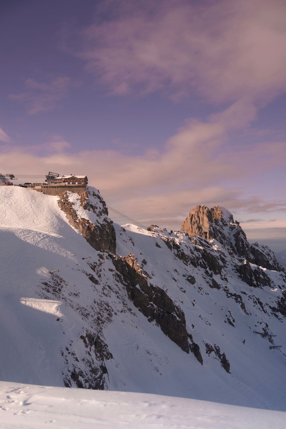 Montagne enneigée et restaurant sur une crête au coucher du soleil.