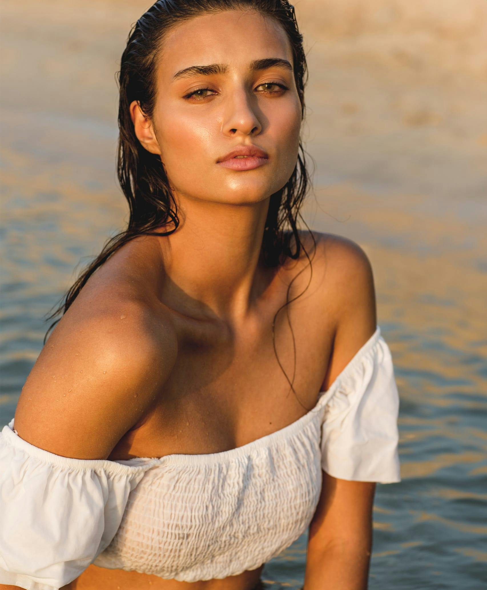 Woman in white off the shoulder crop top near water.