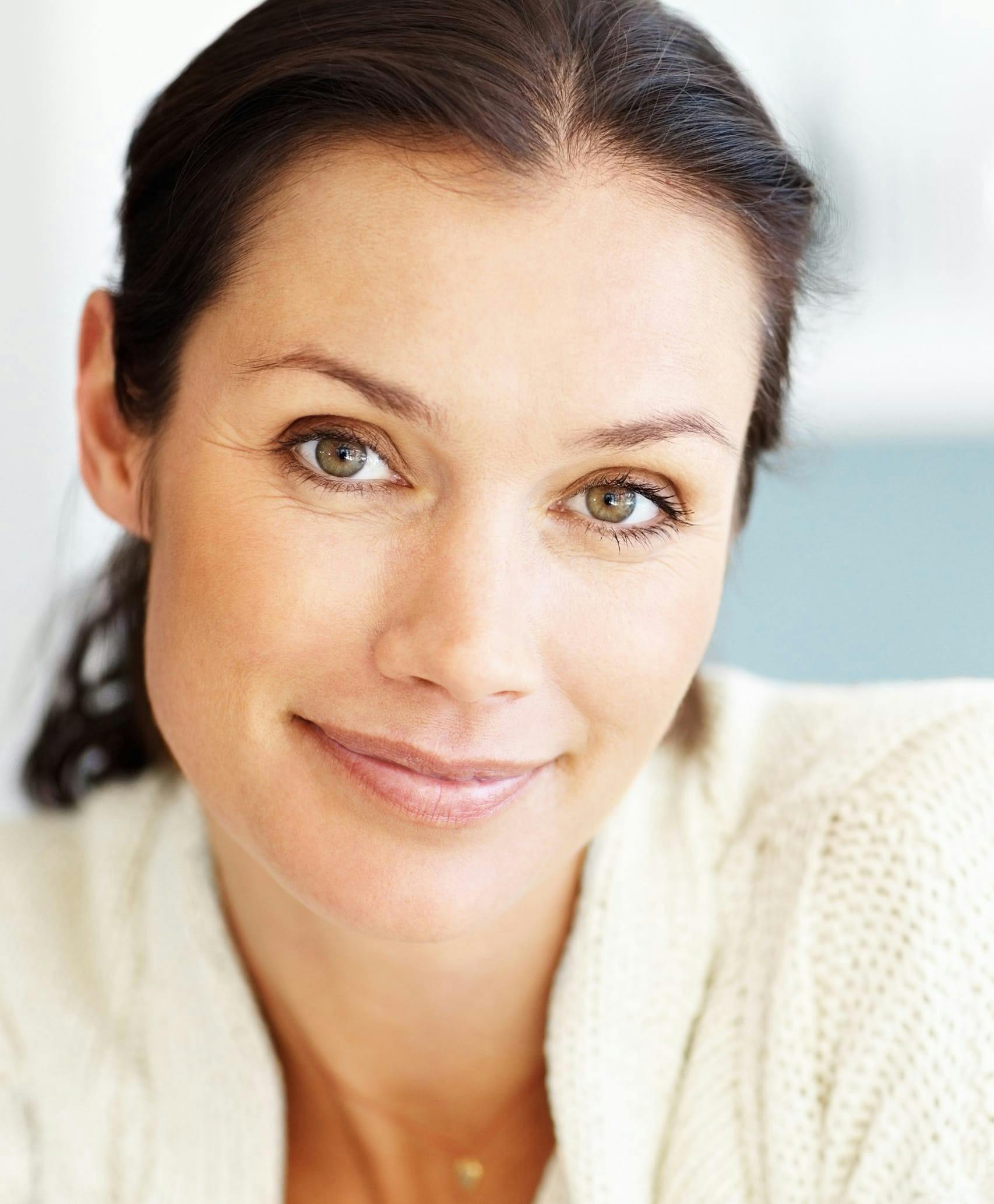 Smiling woman with hair back in white knit cardigan.