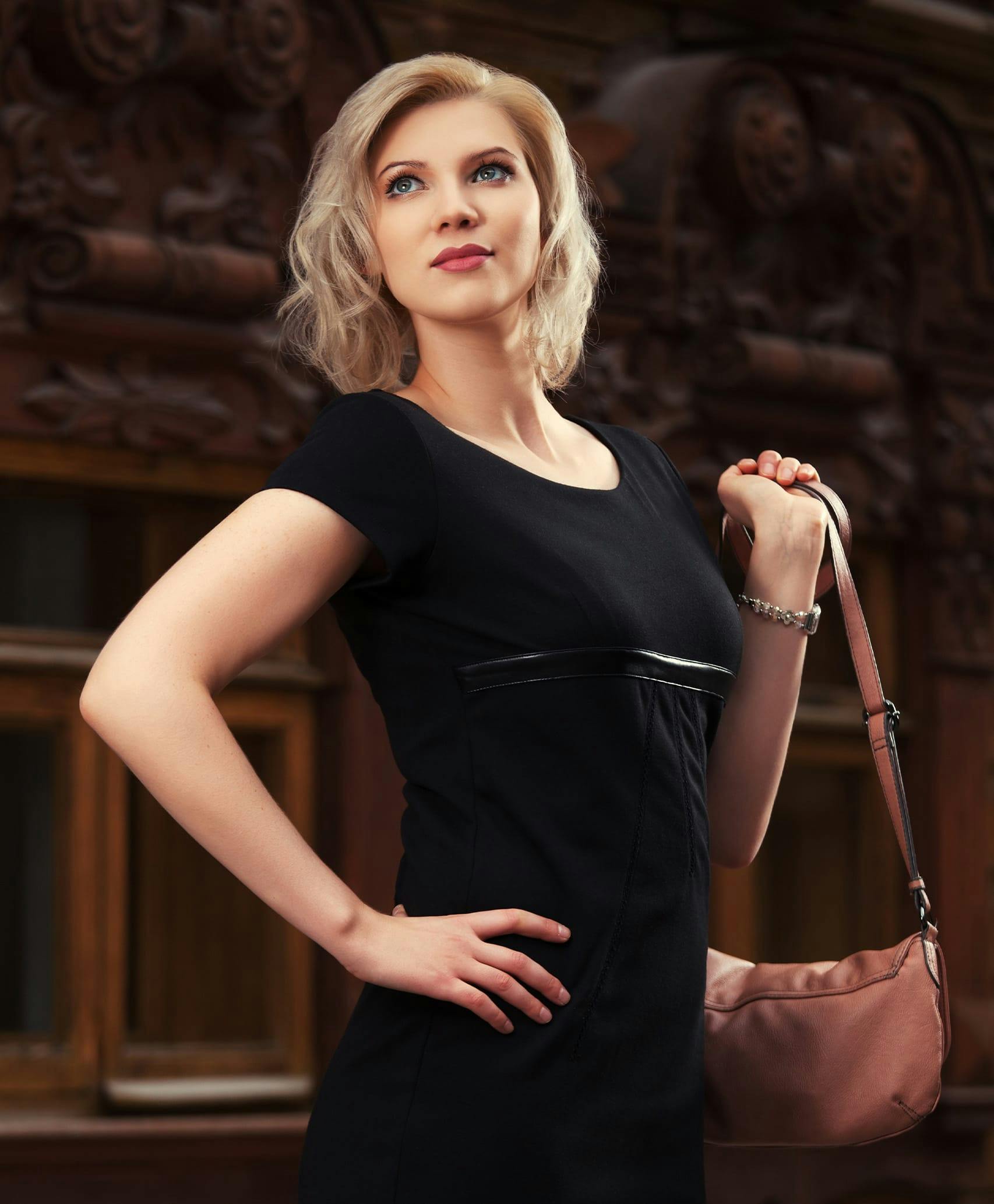 Woman in black dress holding purse in front of ornamental wood feature.