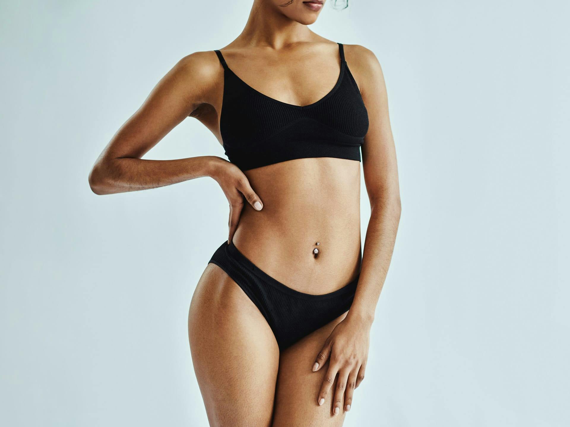 Woman in black two-piece swimsuit with hands on hip and thigh.