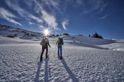 Zwei Personen mit Schneeschuhen im Aufstieg, die Sonne scheint.