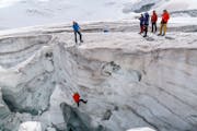 Eine Gruppe von Bergsteigern schaut zu, wie eine andere Person in eine Gletscherspalte abgeseilt wird.