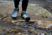 Jemand geht über steinigen Untergrund, im Vordergrund sieht man Wasser.