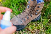Ein Wanderschuh steht auf der Wiese, jemand imprägniert ihn mit einem Spray.