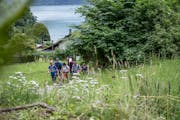A group hikes up a slope, in the background you can see a lake.