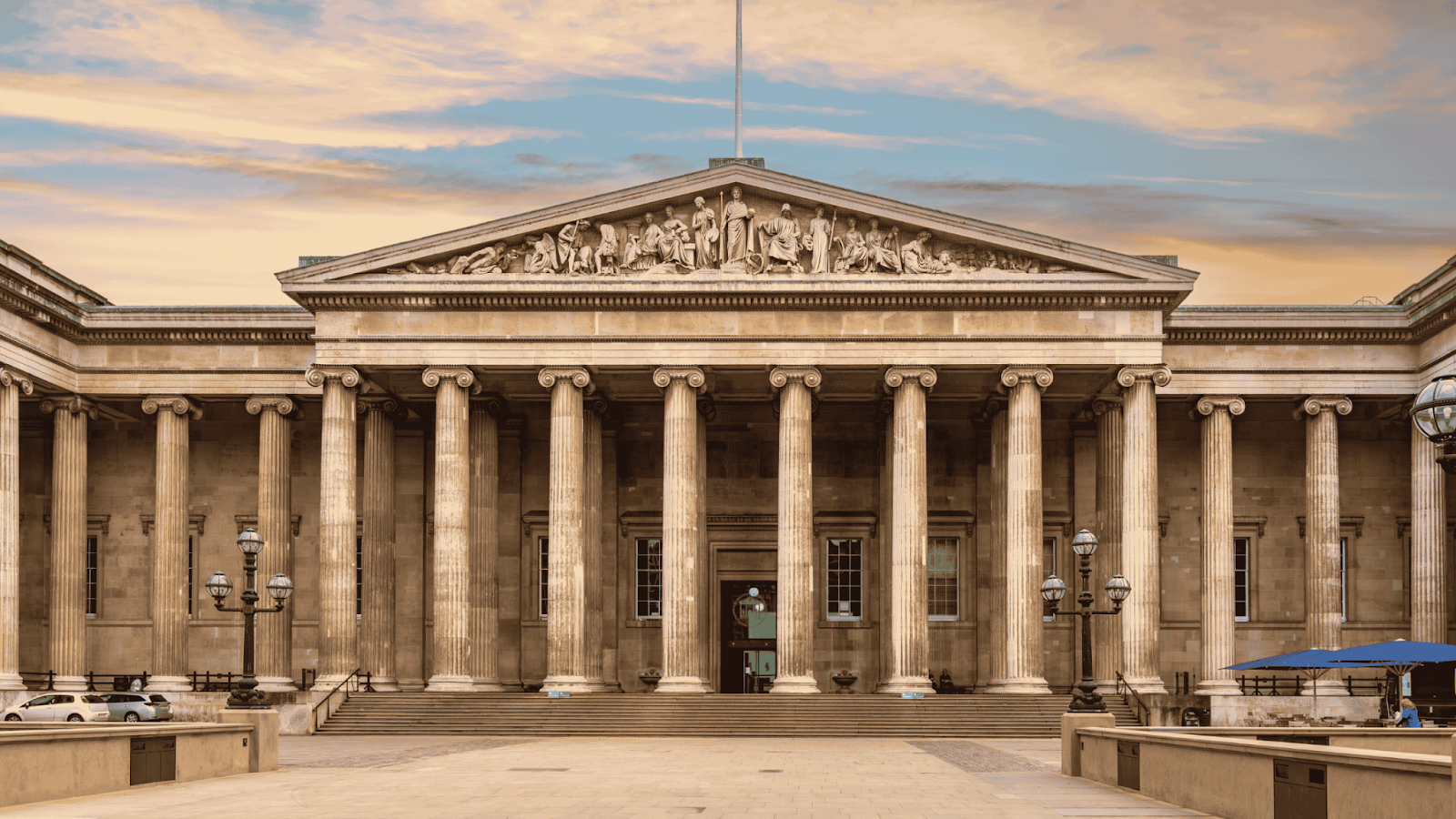 Facade of the British Museum with neoclassical architecture featuring tall columns and intricate pediment carvings, captured at sunset.