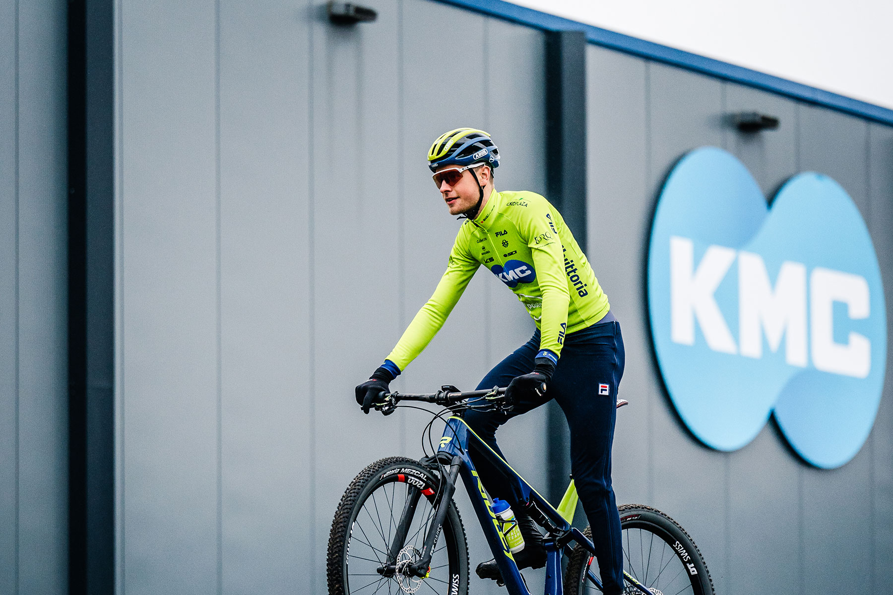 Cyclist from the KMC Mountainbike Team riding the KMC Bike Park. In the background the new KMC building with the large format company logo.