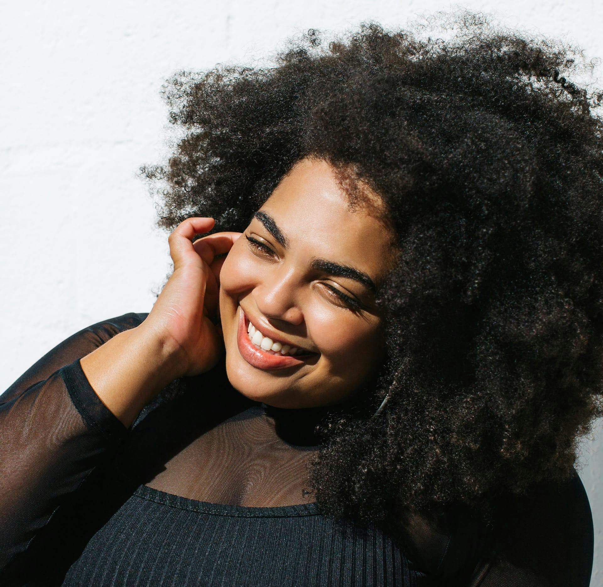 woman with afro smiling with hand on her ear