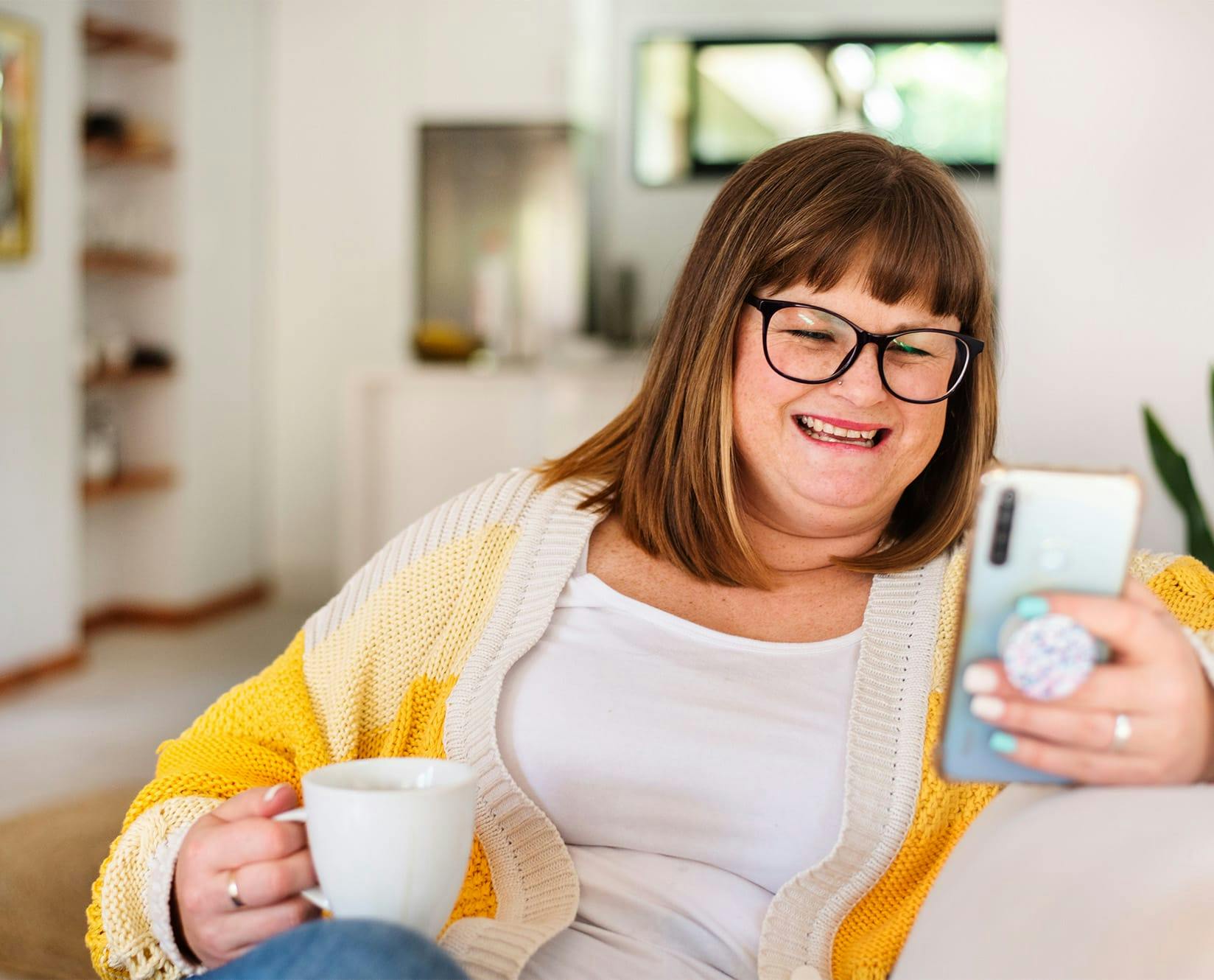 woman holding hold phone and a cup of coffee