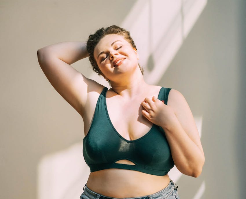 woman with short hair with hand behind her head and hand on her bra strap