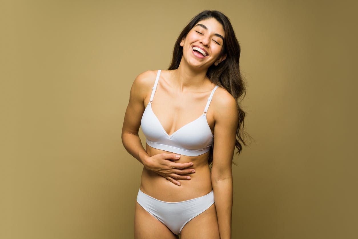 Curvy woman smiling in underwear with her hand on her stomach in studio shoot