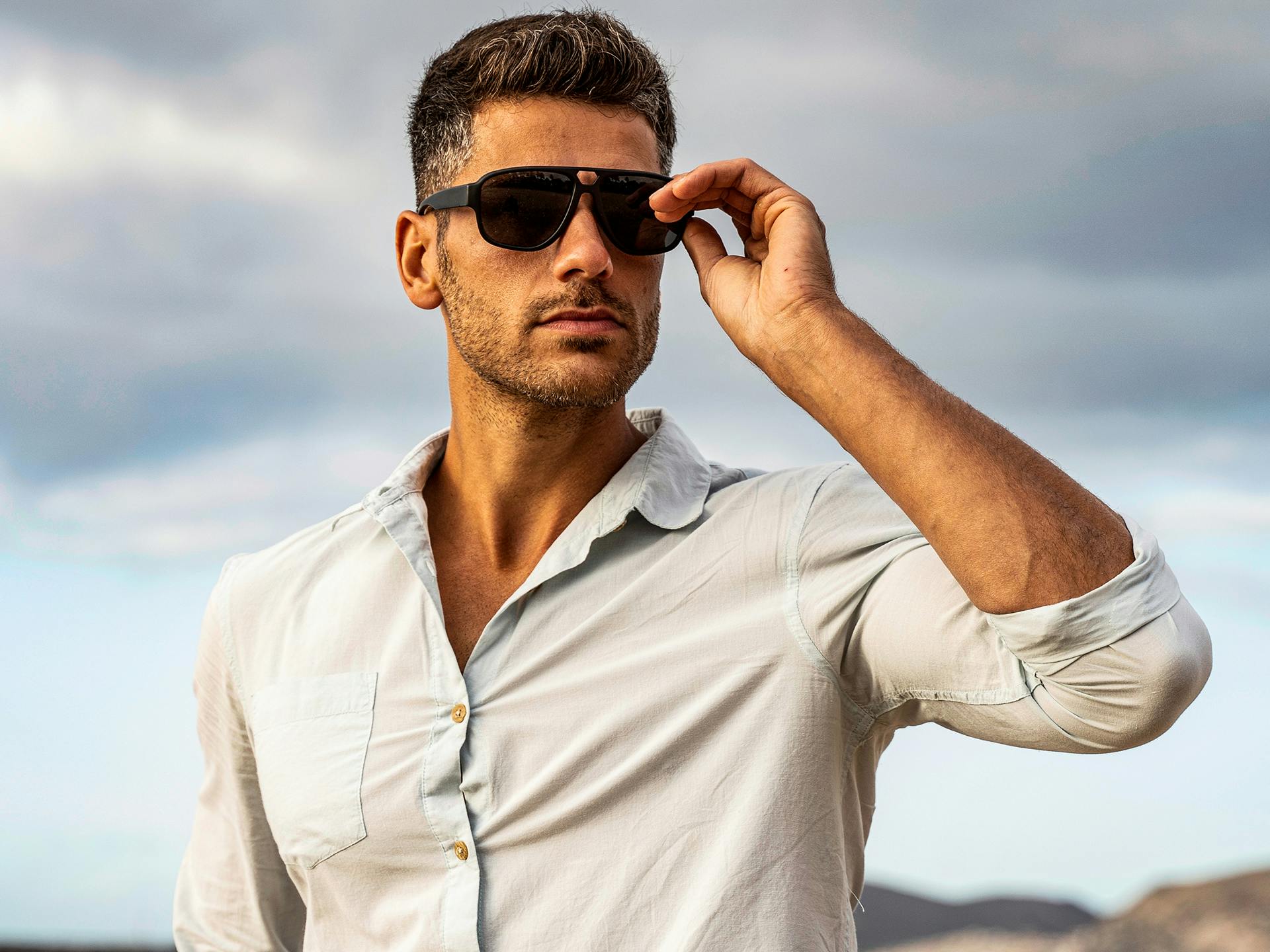 Man in white button up holding sunglasses to face.