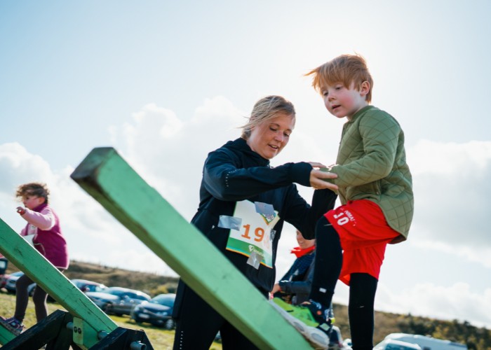 Dette billede viser en mor som hjælper sin søn over en vippebum til Hero Run
