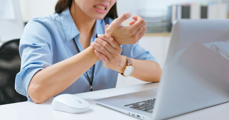 woman sitting in front of a laptop grabbing her wrist in discomfort