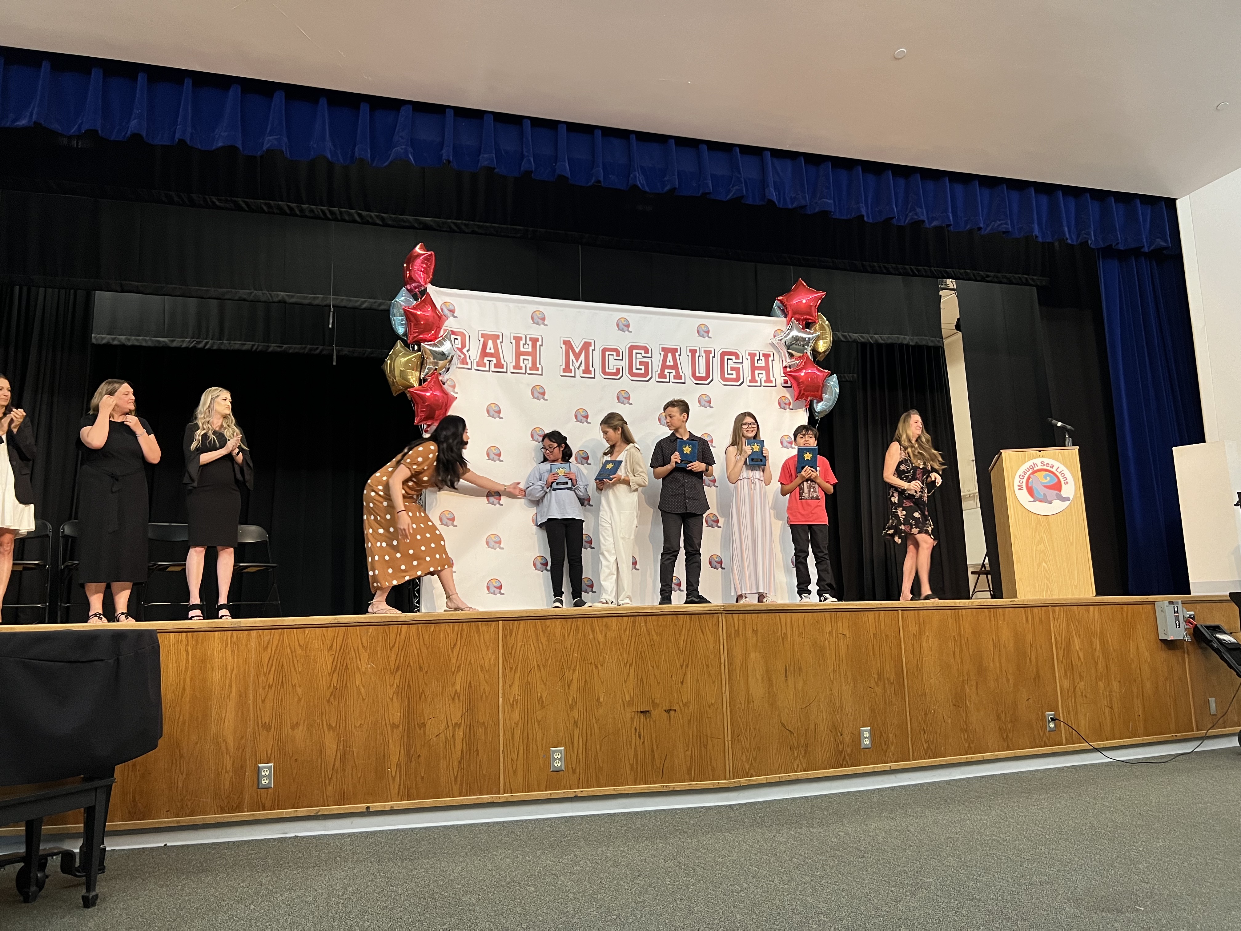 Img: stage, adult, female, person, woman, crowd, shoe, sandal, chair, microphone