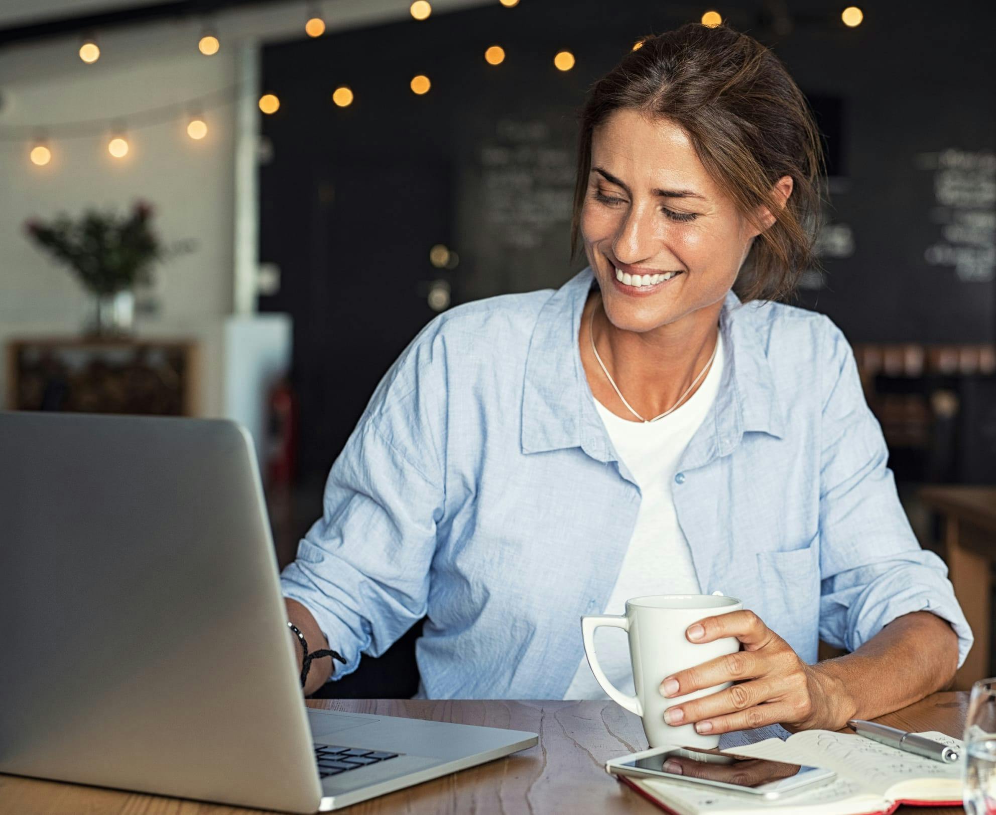 woman smiling while holding a cup and looking at a laptop