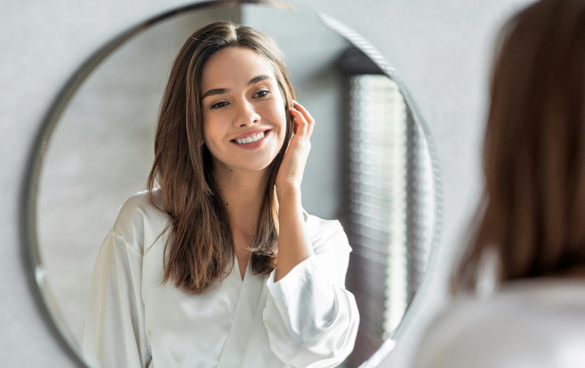 Smiling woman looking at wall mirror.