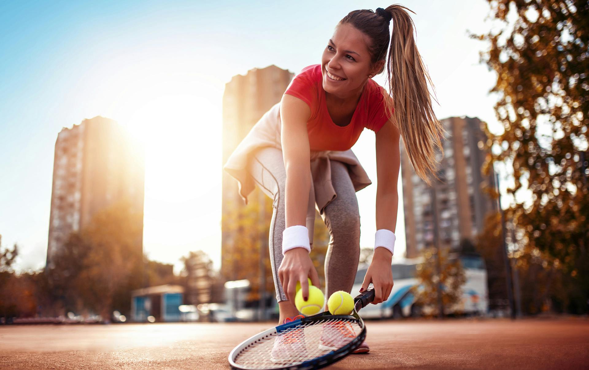 Woman playing tennis with city sunset background.