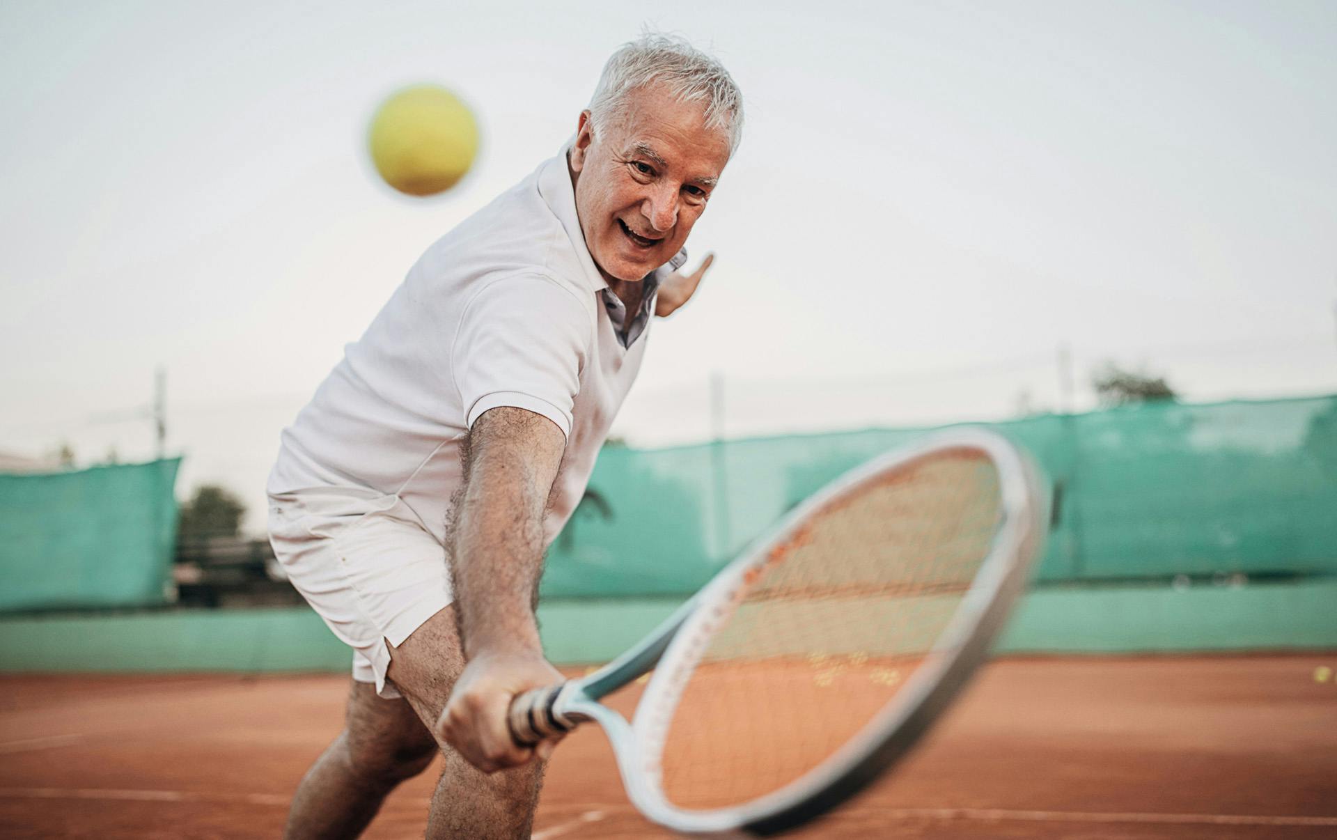 Man hitting tennis ball on clay court.