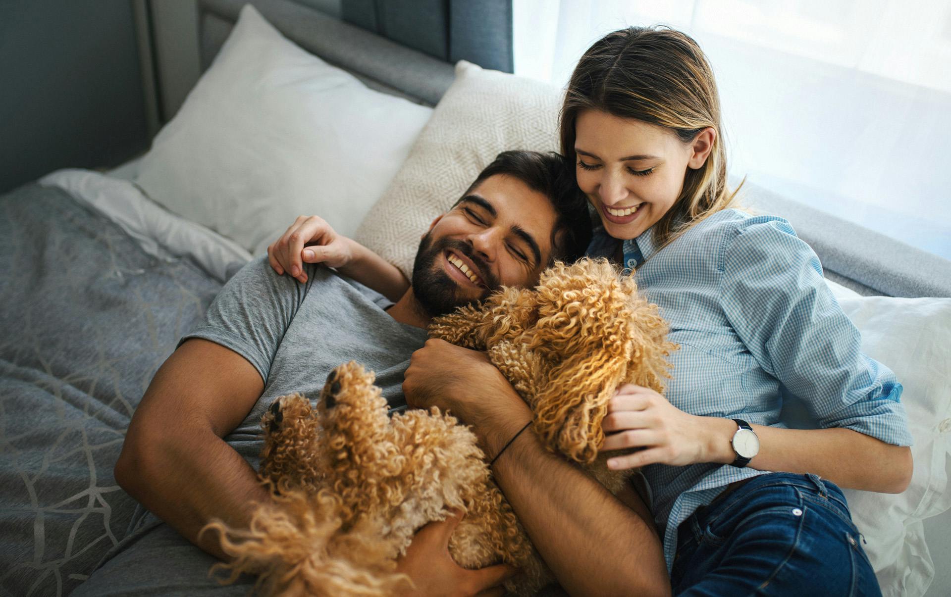 Cupple cuddling with dog in bed.