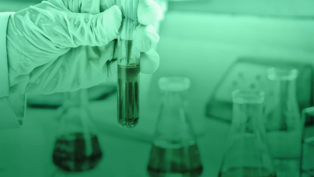 Scientist with gloves holds a glass test tube with liquid inside.