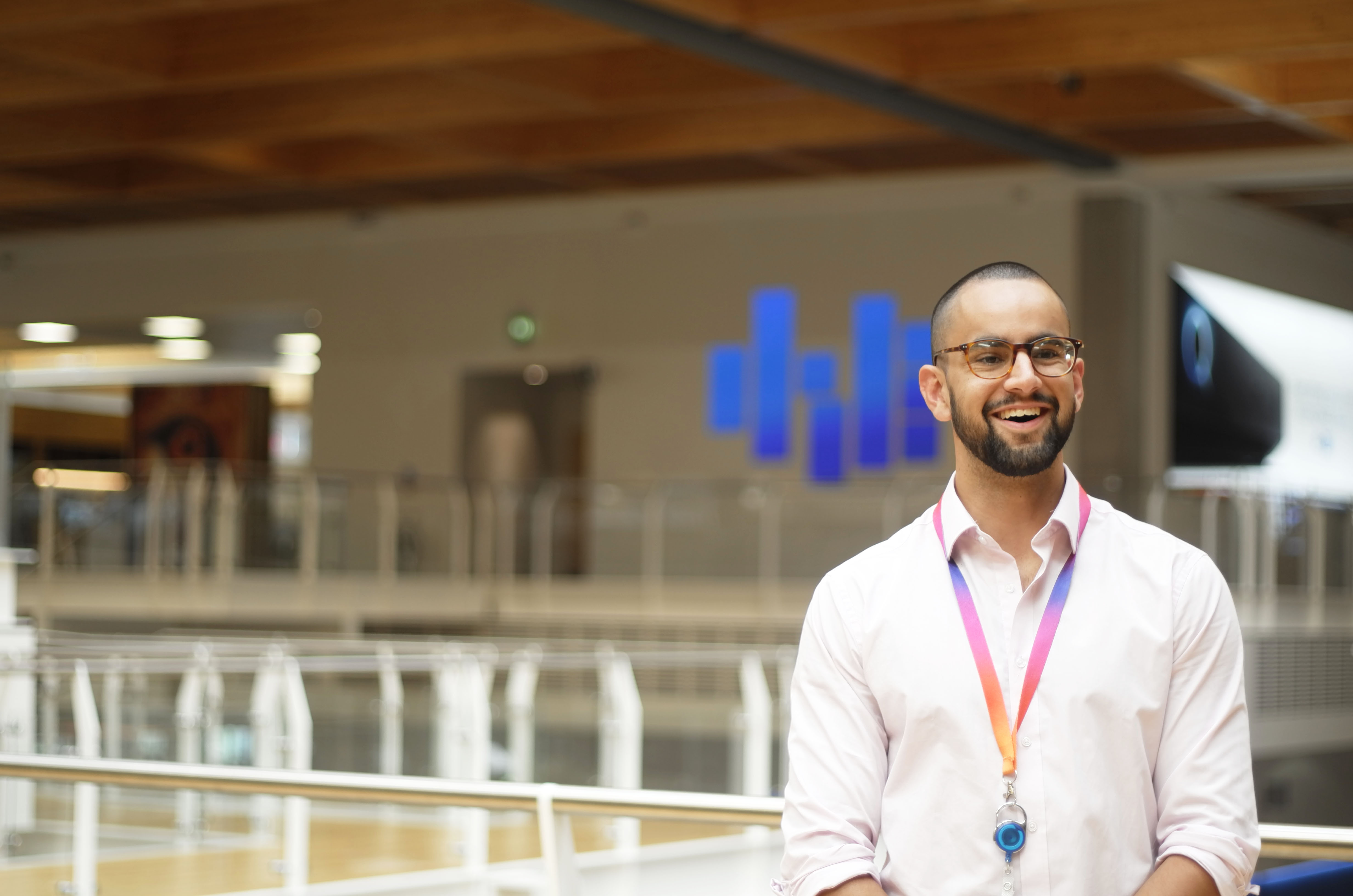 Man in white shirt with colourful lanyard smiling in a bright, modern office atrium.