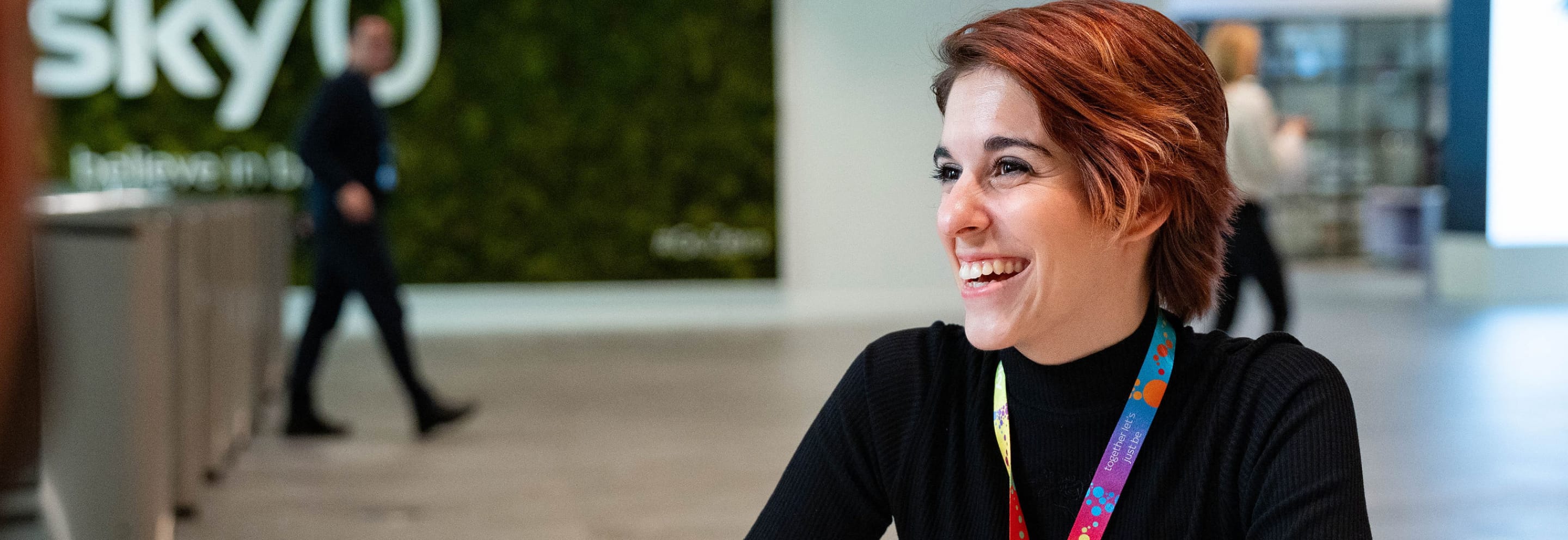 Close up image of female with red hair wearing a branded sky lanyard.