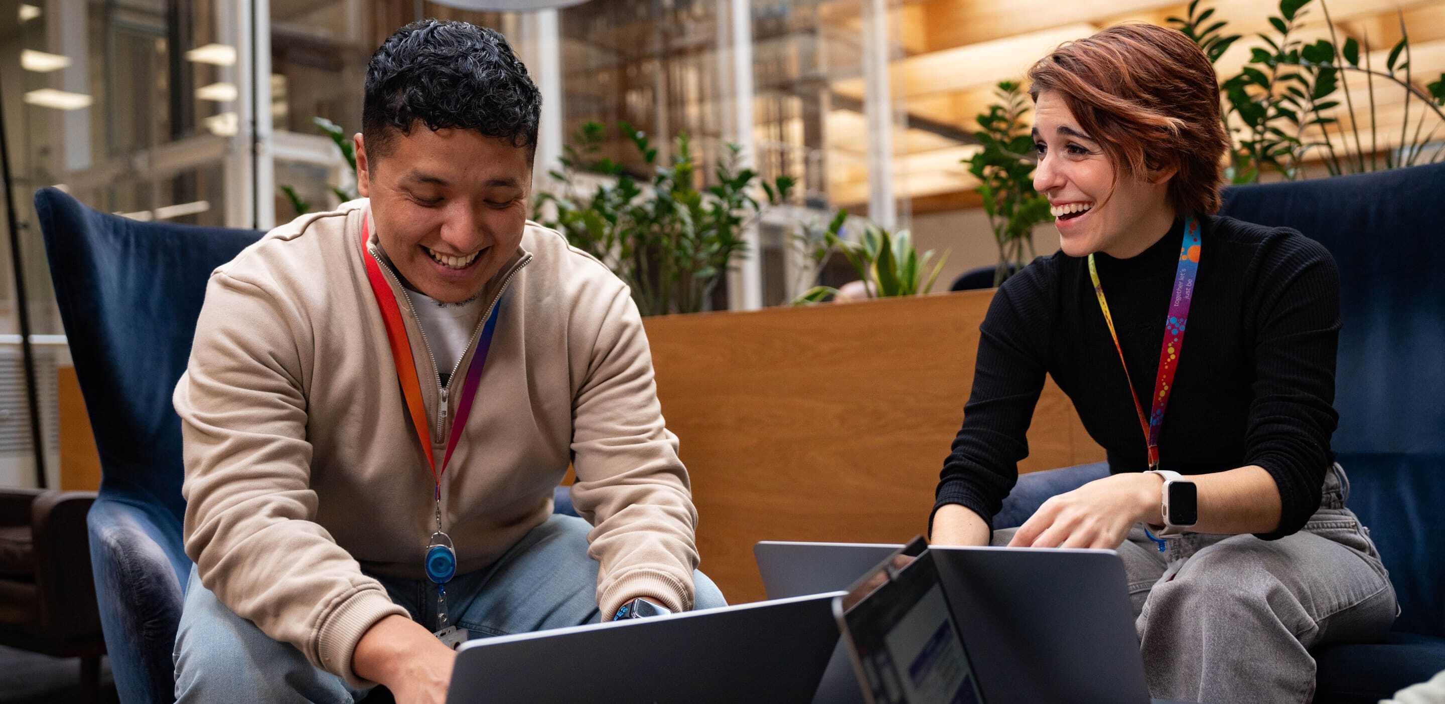 Two people laughing together whilst on laptops