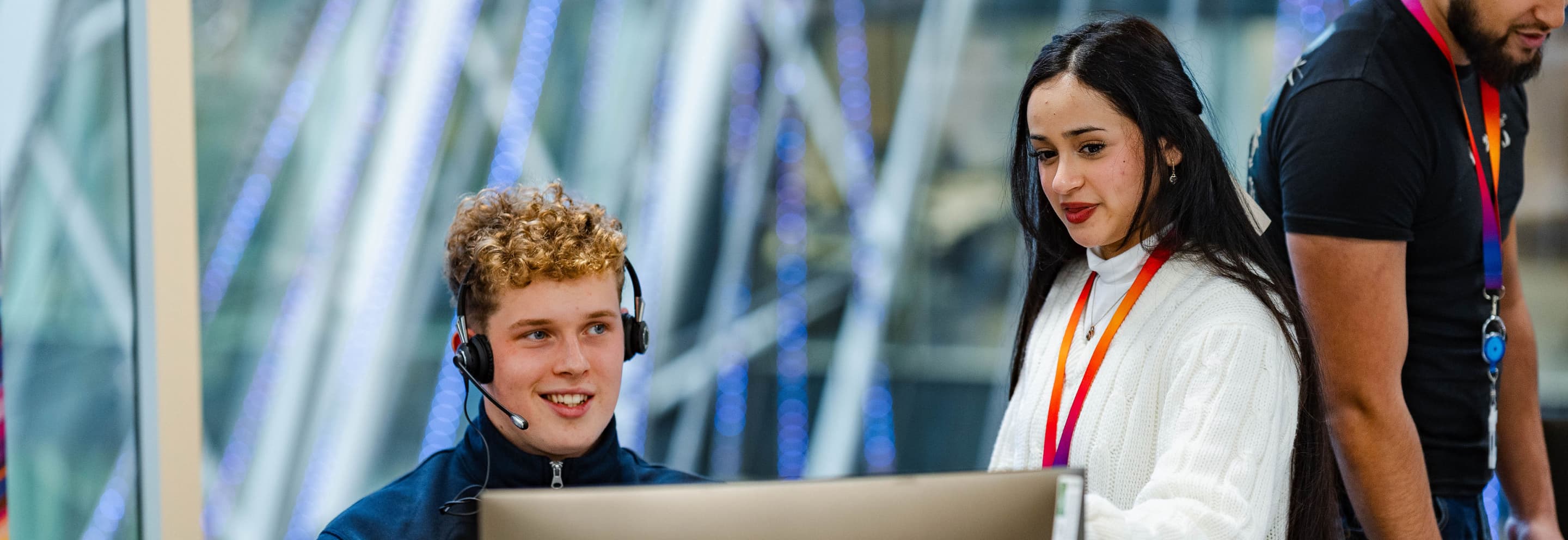 man with headset looking at a screen with a woman standing beside him