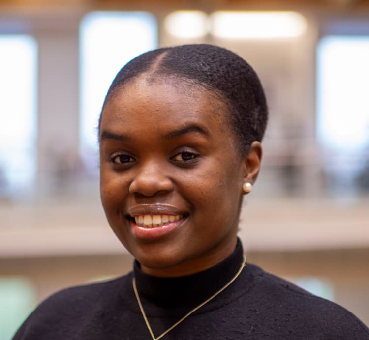 a smiling black woman with her hair in a bun and wearing a black turtleneck top