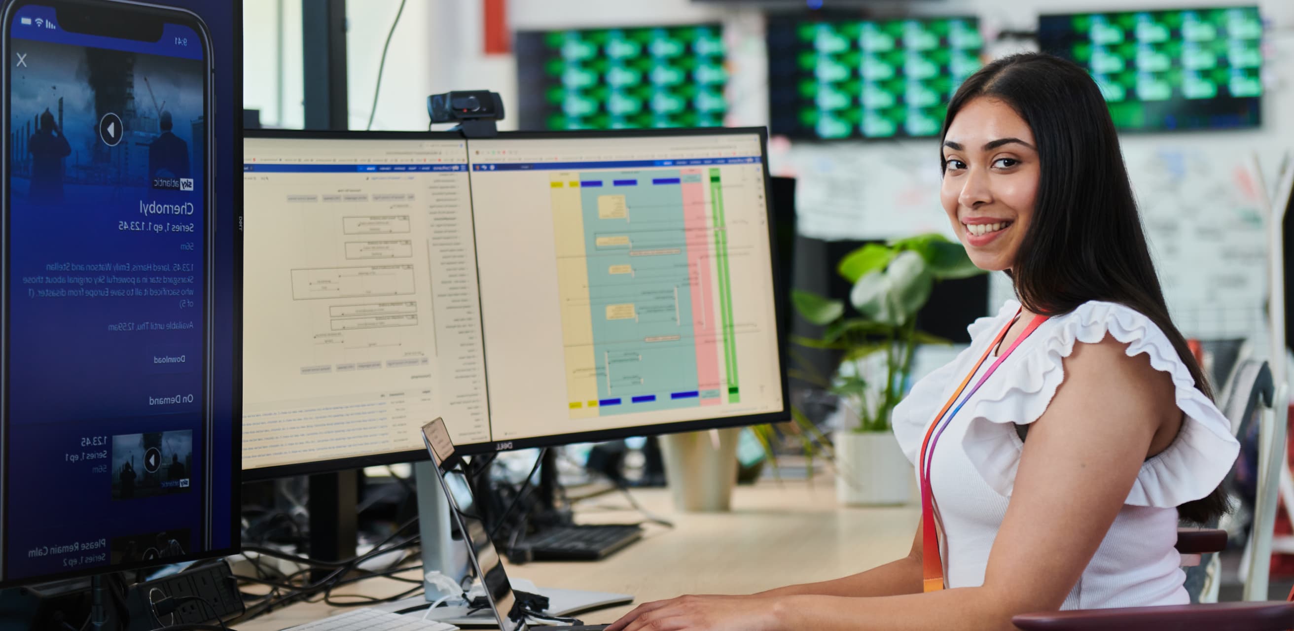woman with long black hair in a white blouse working from multiple monitors