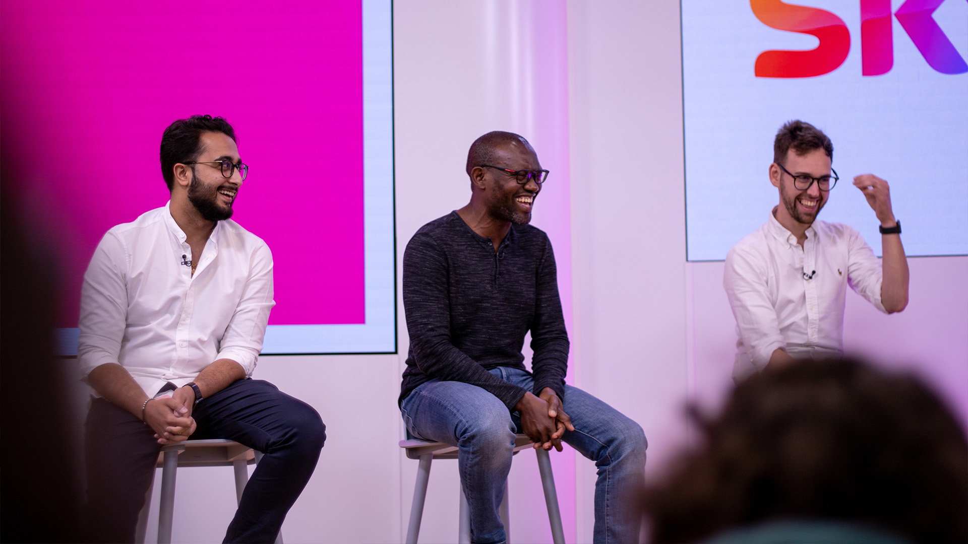 Aman and his colleagues deliver a speech to an audience of Sky colleagues. The room is busy, as Aman and colleagues laugh at one of the panelists jokes.
