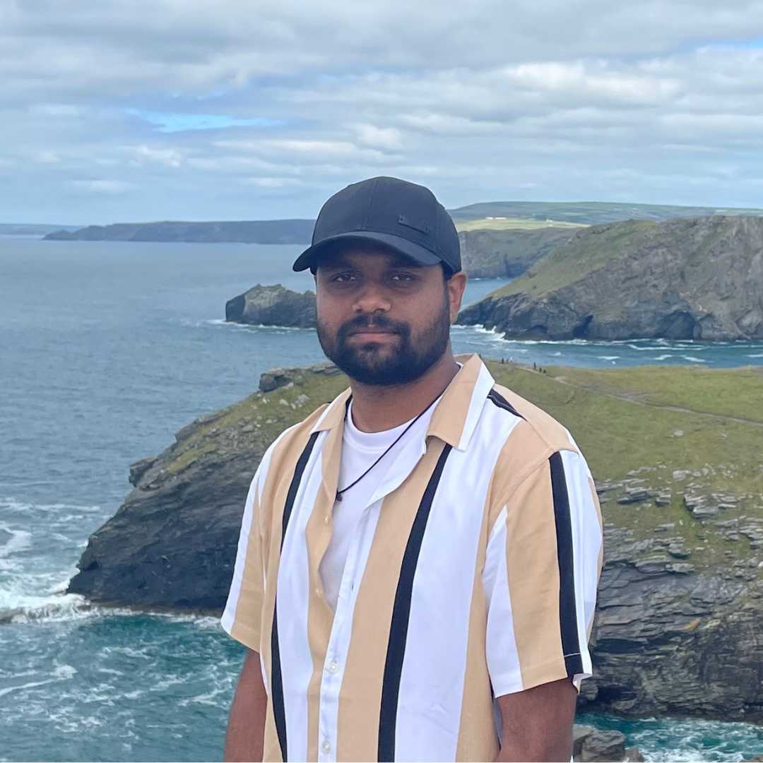 Gokul standing near the coast wearing a black hat with a brown and black striped shirt