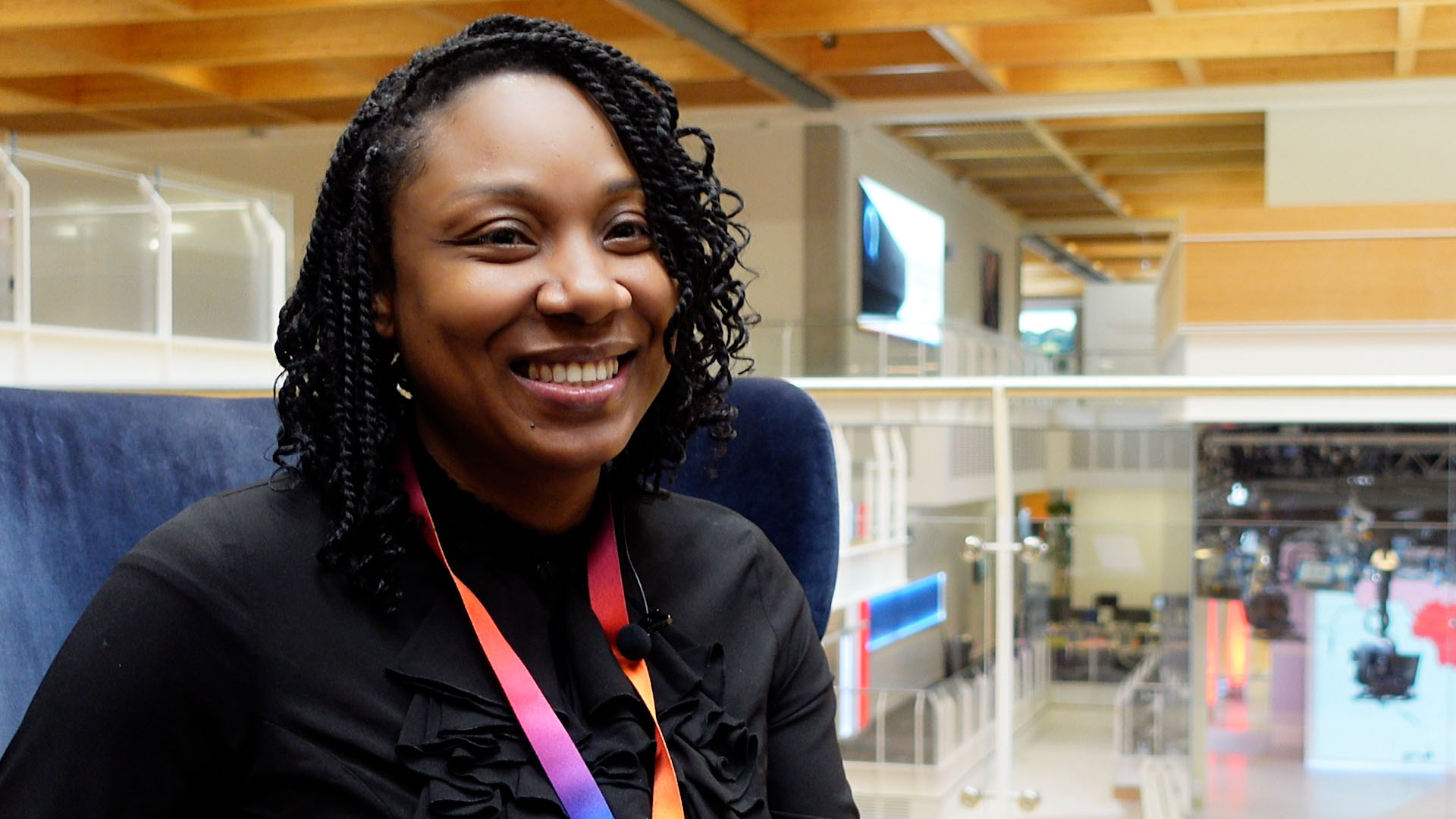 Malissa looks off to the right of the camera smiling. In the background is the Sky News box in our HQ in Osterley - with level one and two walkways visible in the background.