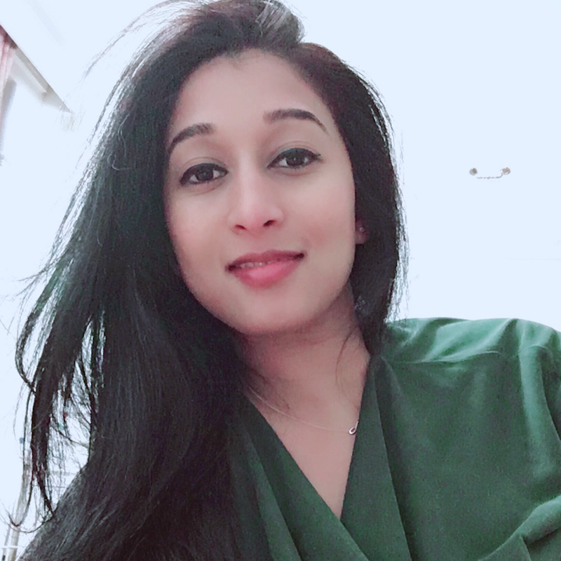 A selfie of Ruchira. Ruchira is looking directly into the camera, wearing a green top.