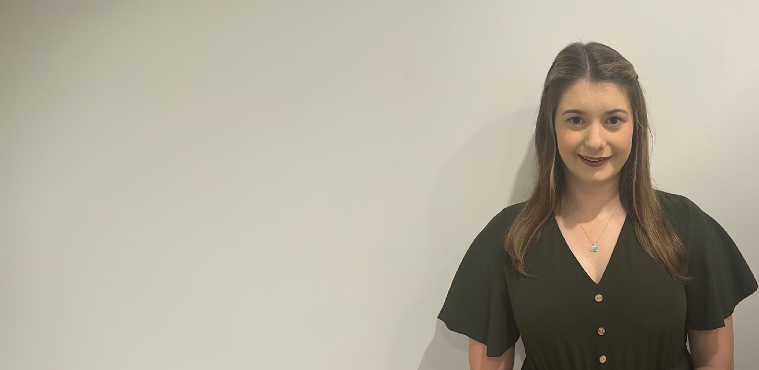 Woman with straight brown hair smiling at the camera against a plain off-white background.