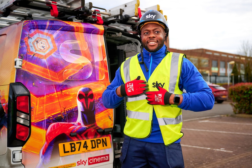 Male field engineer wearing safety gear stands confidently in front of a colourful Sky Cinema van featuring superhero artwork.
