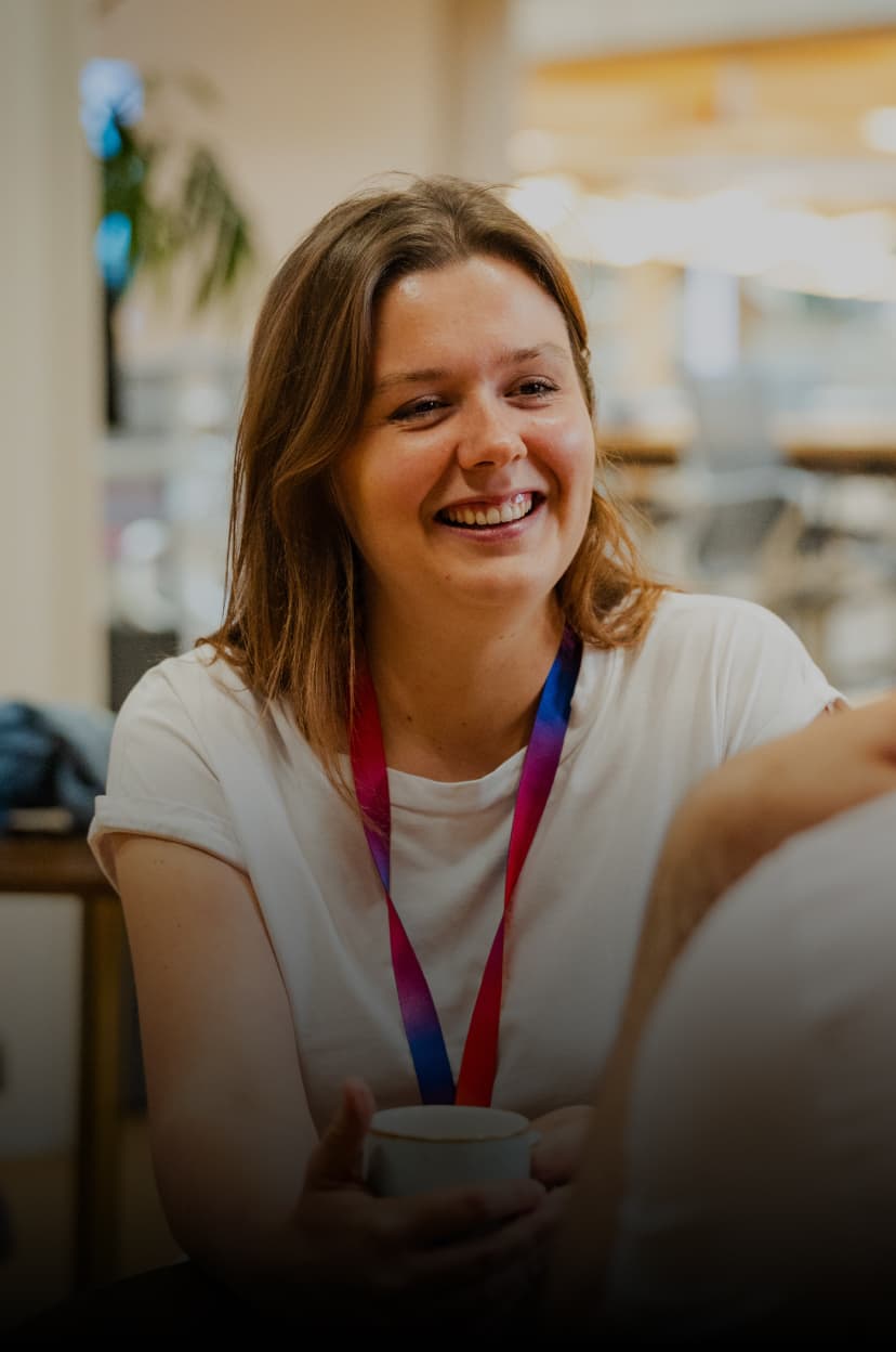 Woman smiling and holding a mug in a casual conversation at a table in a modern office café.