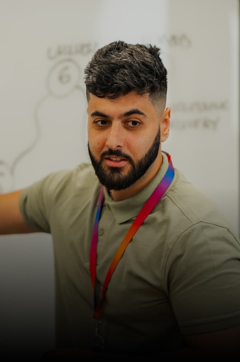 Man in a green polo shirt pointing at a whiteboard during a presentation or meeting.