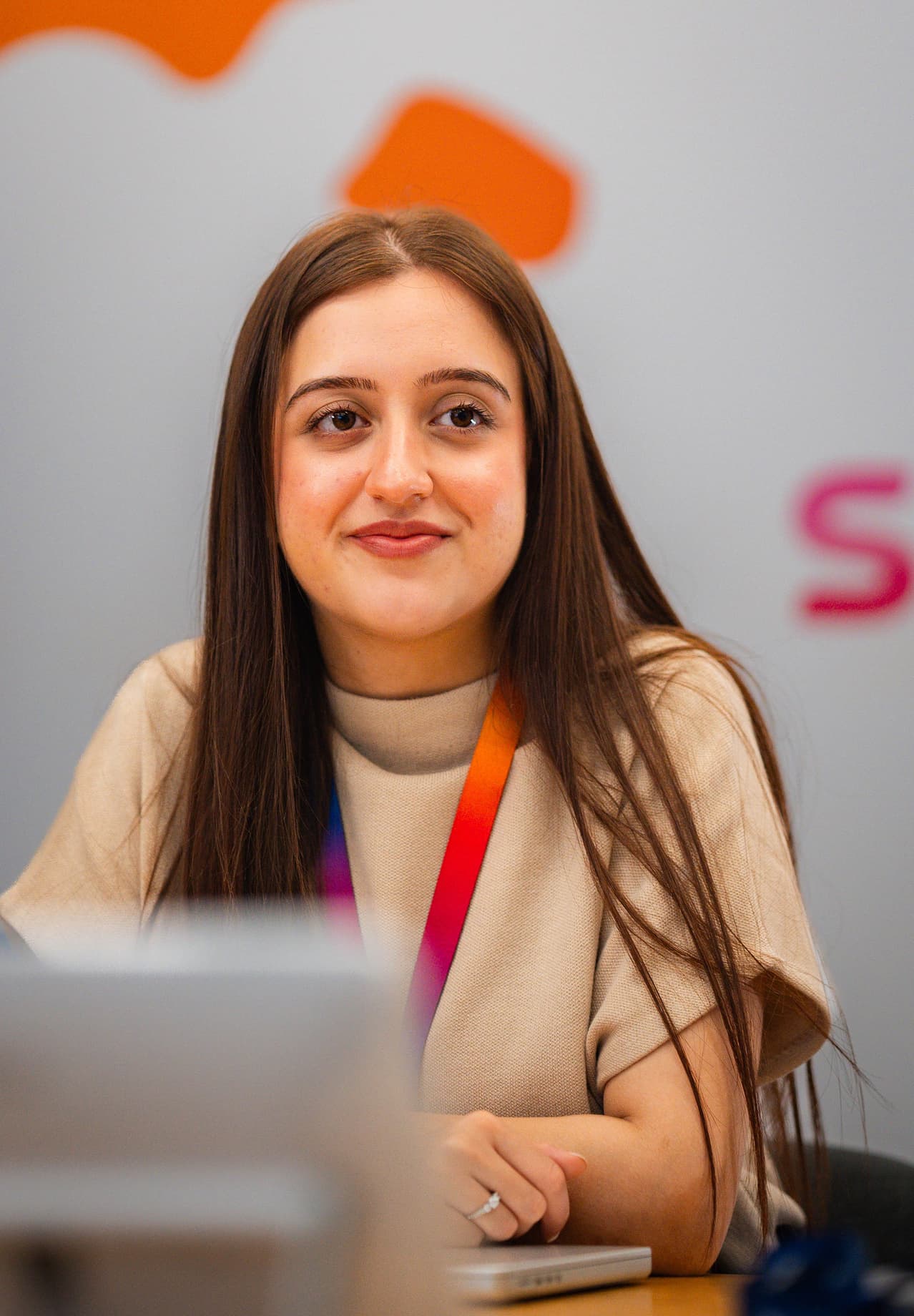 Smiling woman with long hair holding a water bottle and laptop, wearing a Sky lanyard in a modern office.