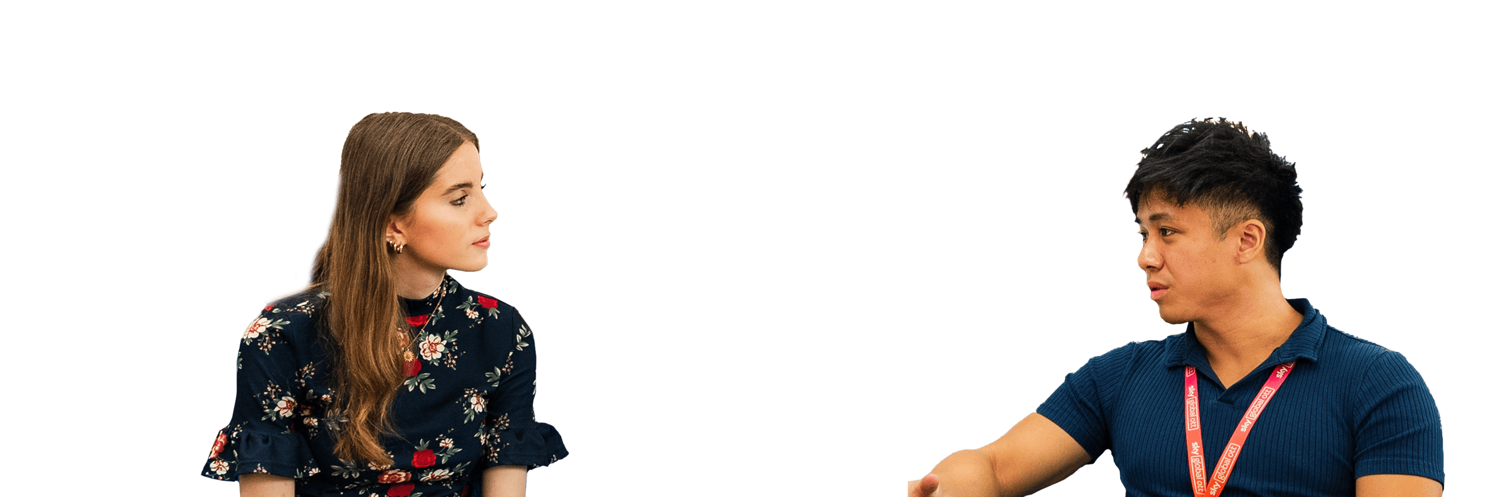 Two colleagues seated and talking, one in a floral top and the other in a navy shirt with a red lanyard.