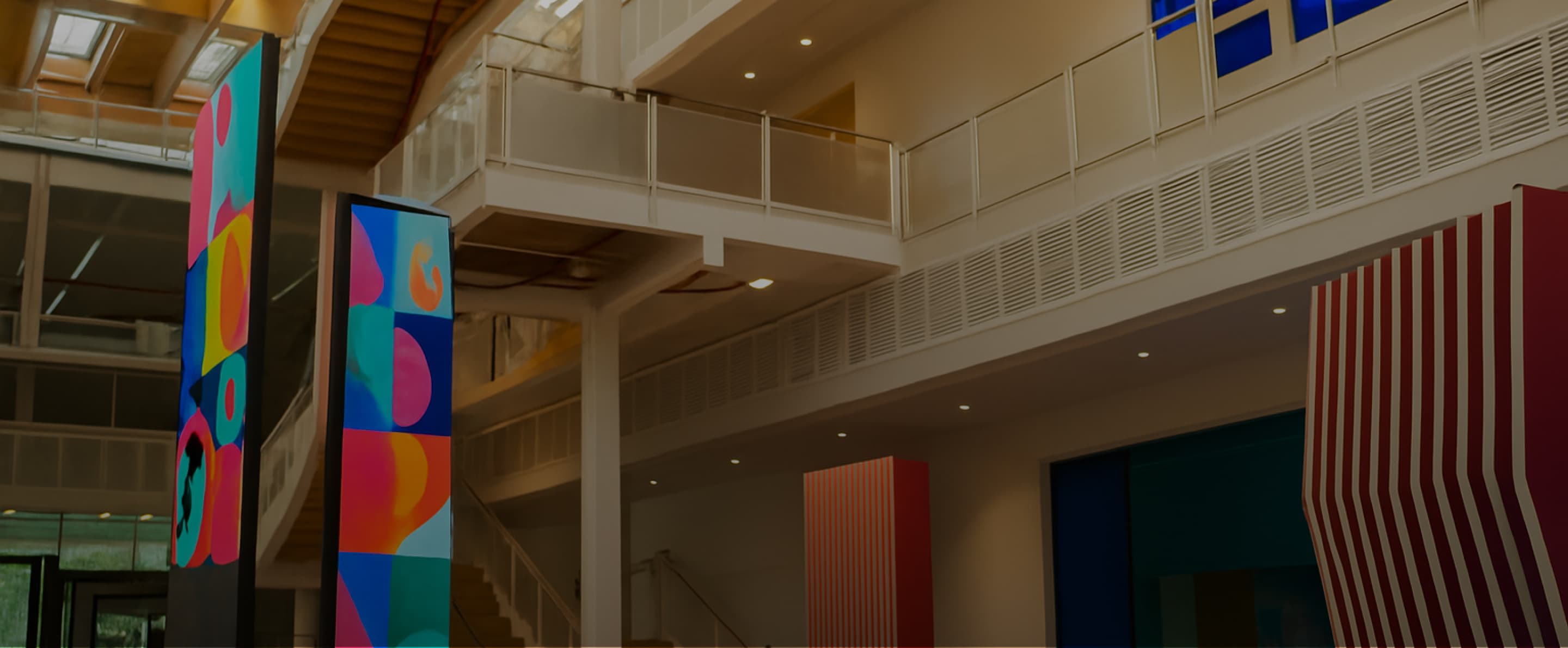 Spacious modern atrium with glass panels, colourful digital columns, and red-striped wall decor.