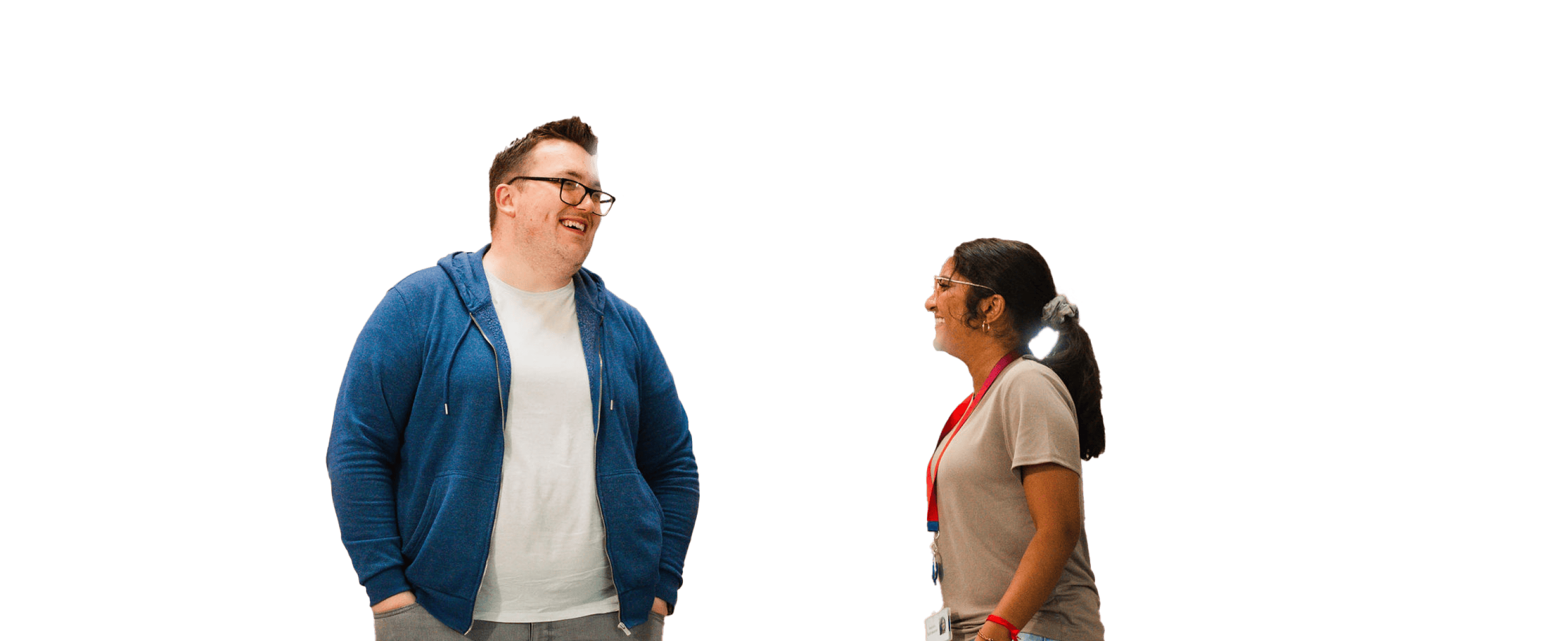Man in blue hoodie and woman with long ponytail smiling at each other on a white background.