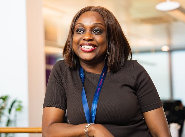 Woman wearing a dark top and Sky lanyard smiling warmly in a bright modern office.