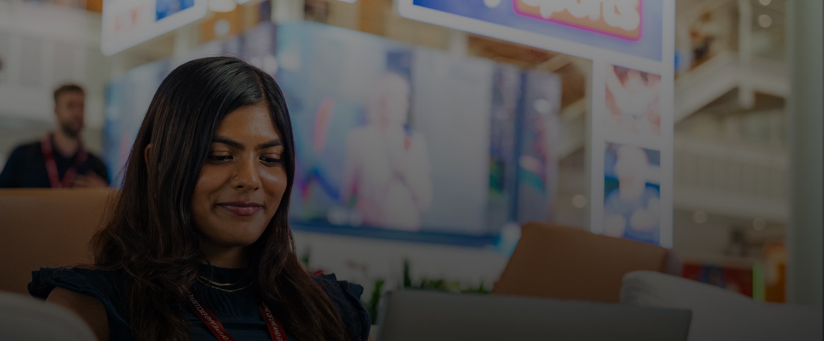 Woman wearing a Sky lanyard works on a laptop in a modern office with screens and lights in the background.