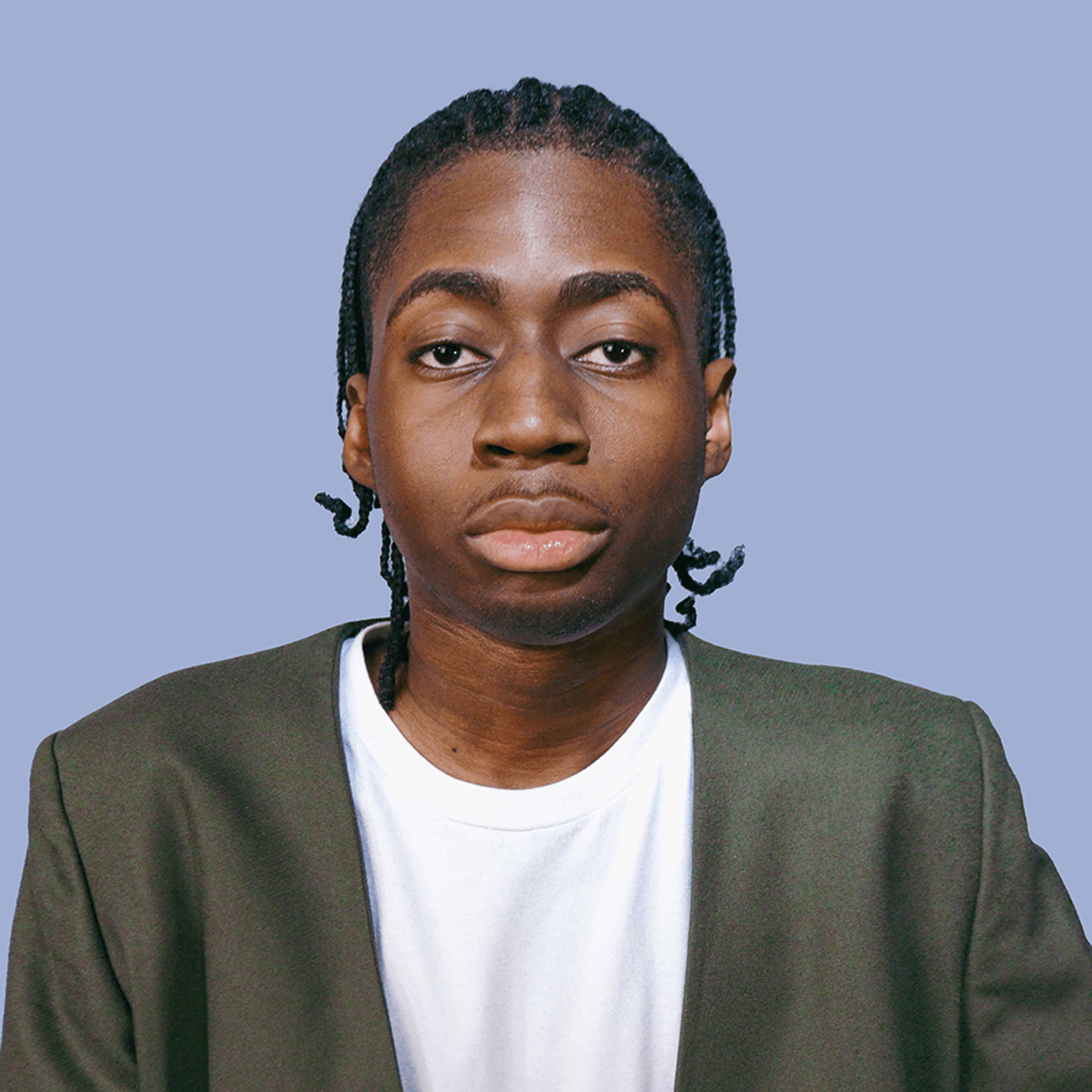 Demi wearing white T shirt and olive green jacket infront of a blue background.