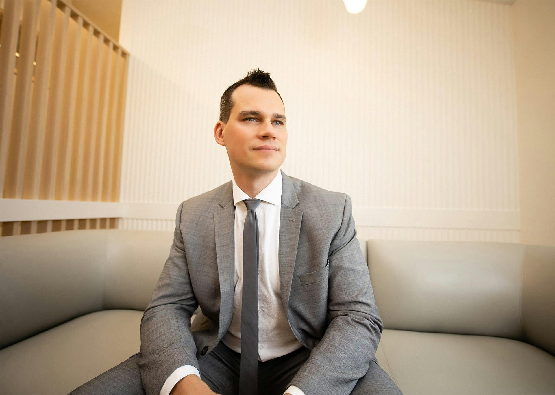 Dr. Brace in suit sitting on couch looking away